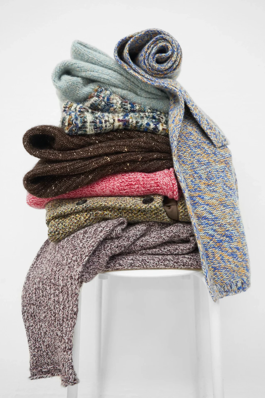 Folded and rolled scarves on a white stool
